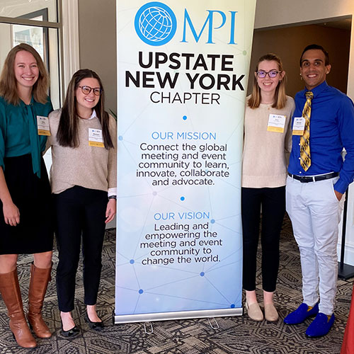 Meeting International Club members standing by a sign.