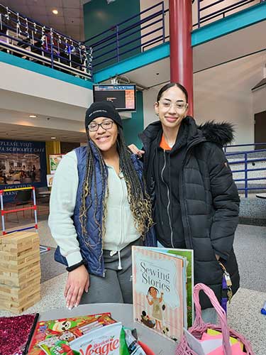 Two students standing at a table in the commons with books and snacks on the table. 