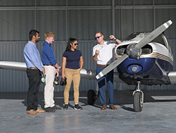 Three students talk with an instructor in front of a College' airplane. 