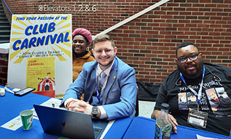 Three students in front of the Club Carnival sign.