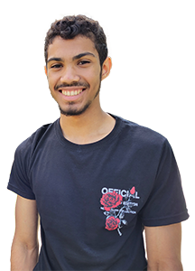 Male student with dark hair and facial hair wearing a black tee shirt. 