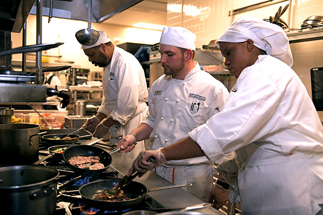 Three students working over the stove in the food prep lab.