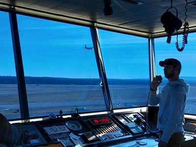 Student working in the Schenectady County Airport Control Tower, a plane taking off outside the window.