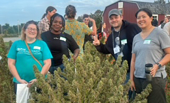 Cannabis student standing around a large hemp plant. 