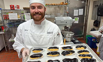 Student holding a tray of chocolate coated eclairs.